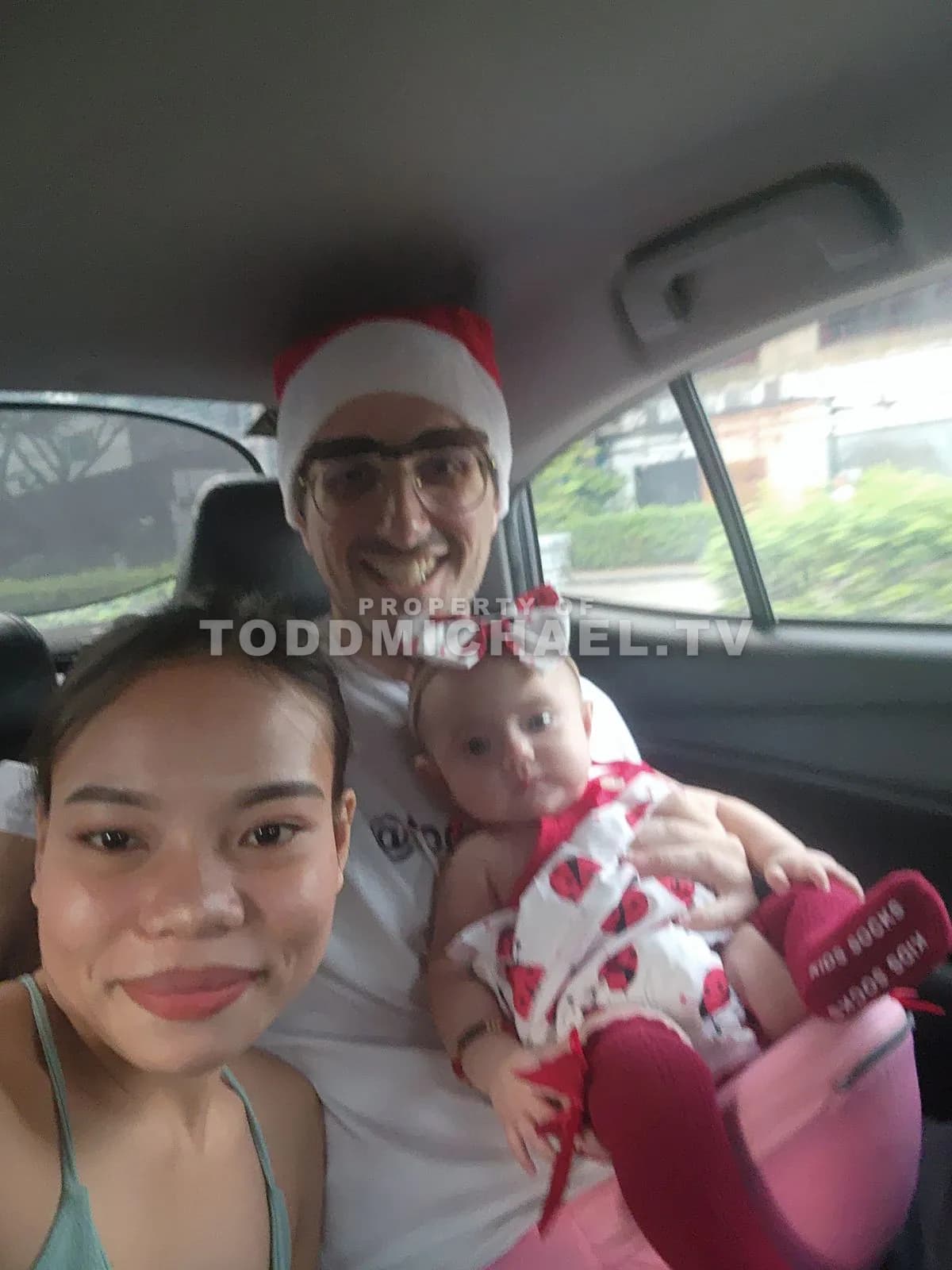 A family of three in a car with a baby wearing festive attire.