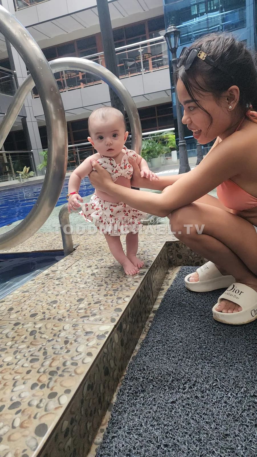 A woman and a baby playing near a pool with metal handrails, captured at 10:17:31.