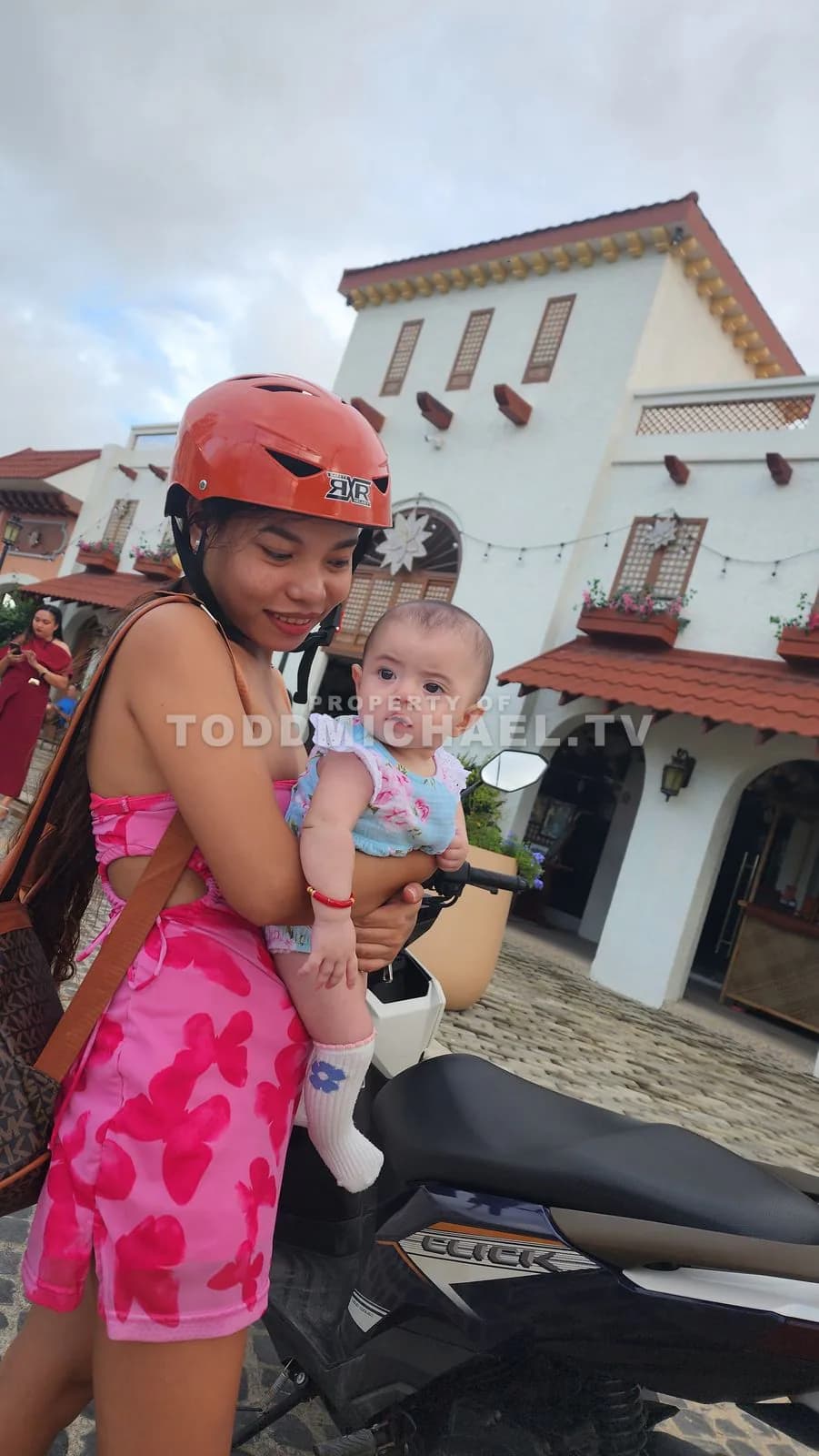a woman wearing a helmet carrying a baby on her back while riding a motorbike.