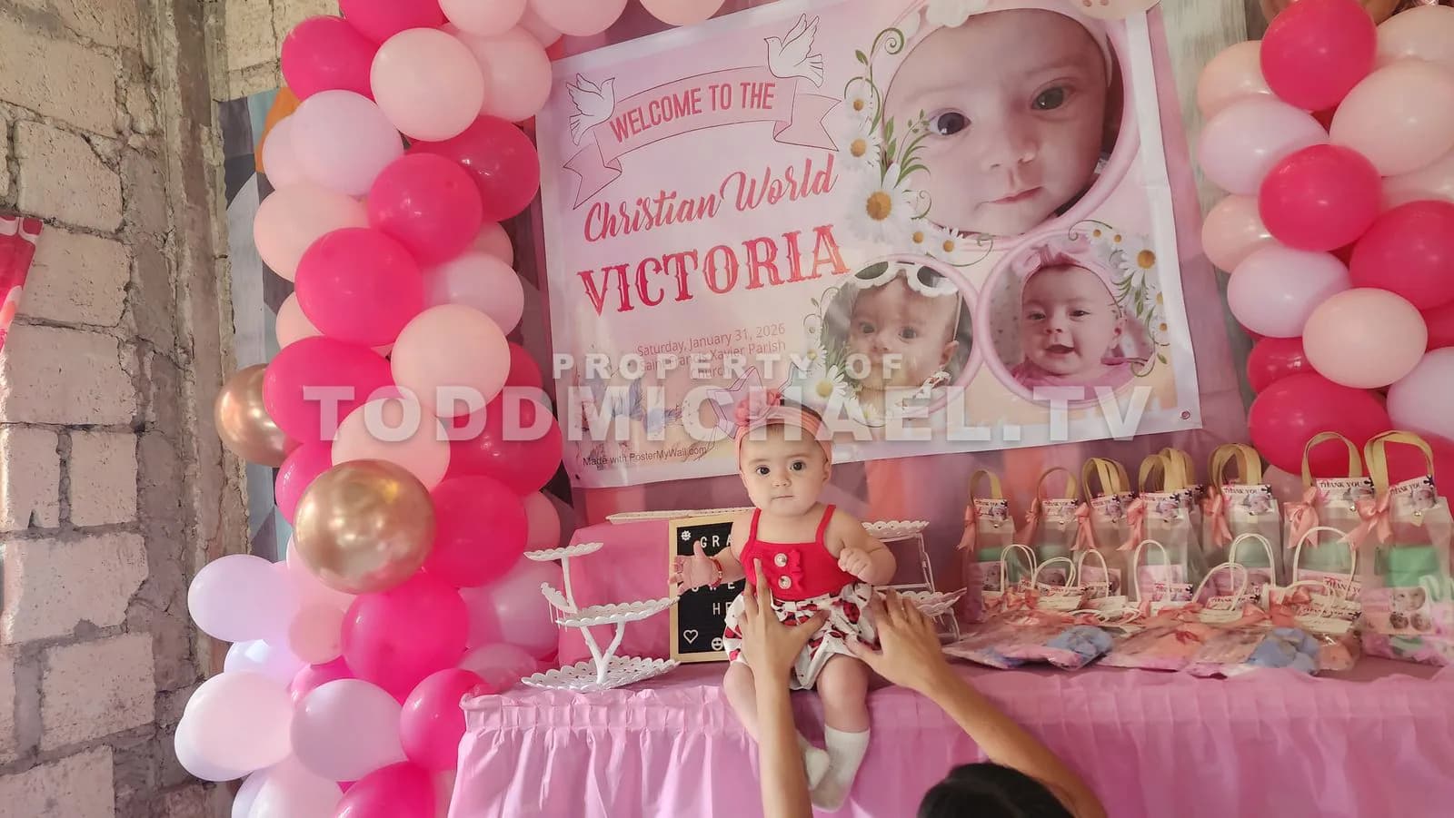 A baby sitting in front of a decorated table with balloons and a banner welcoming Victoria.