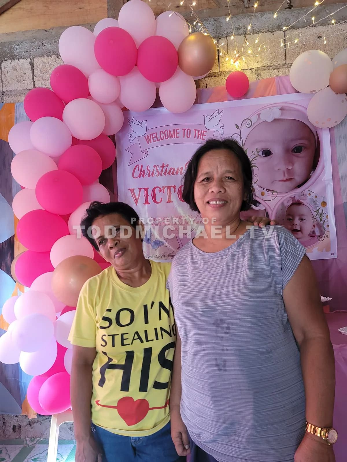 Two women standing in front of a birthday backdrop with balloons and decorations.