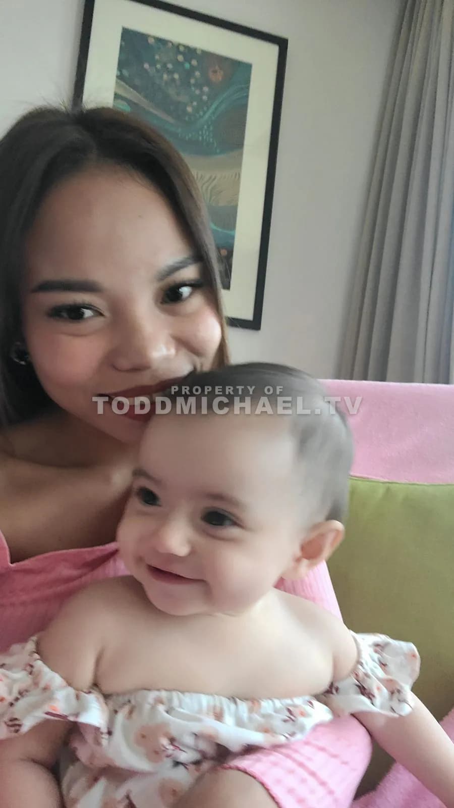 a woman holding a baby while sitting on a couch with artwork visible on the wall.
