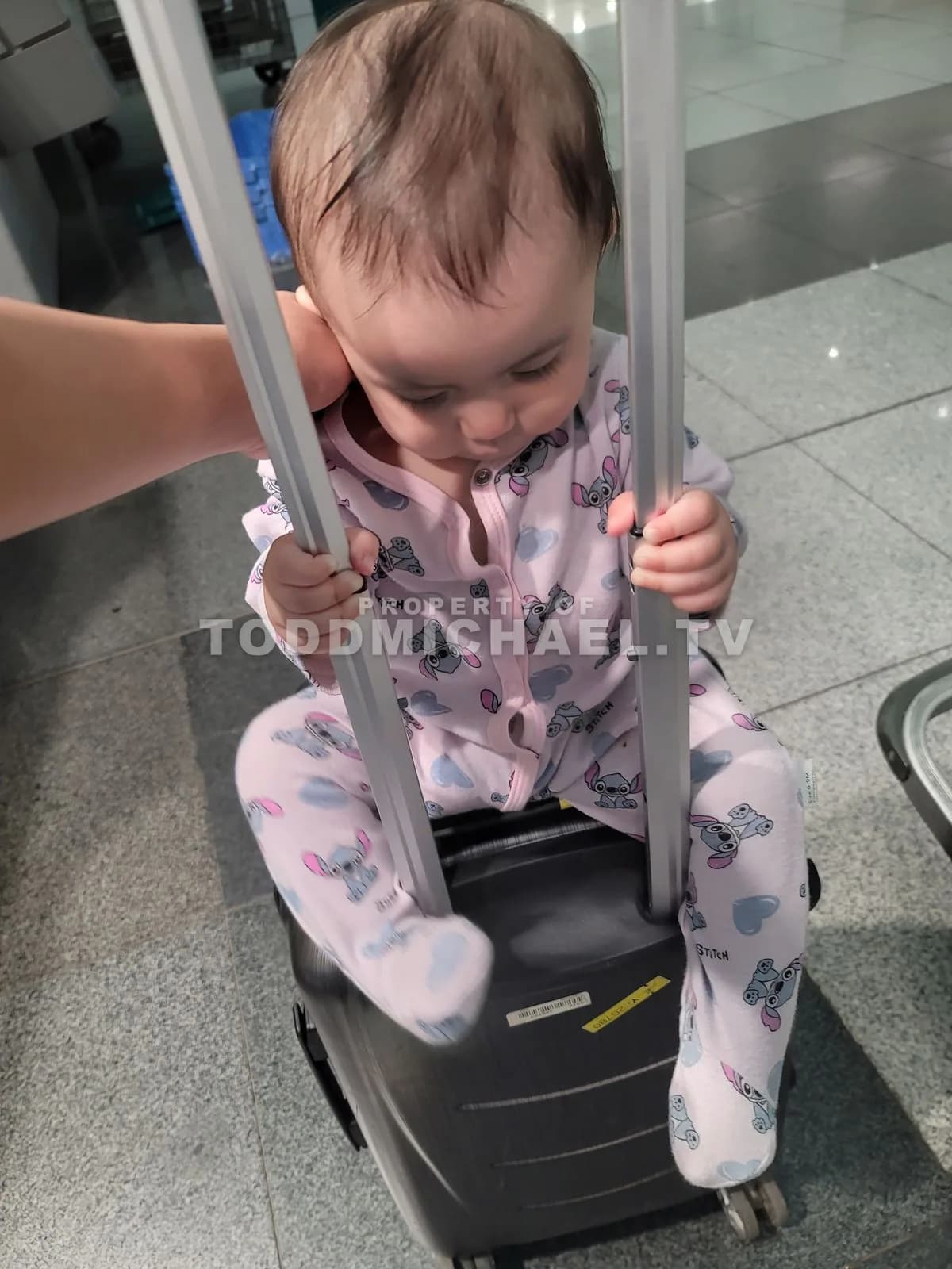 a baby sitting on a suitcase at an airport gate, waiting to board.