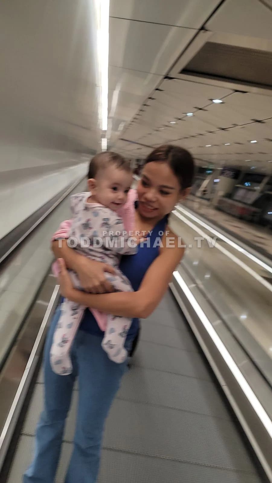 A woman holding a baby on an airport moving walkway.