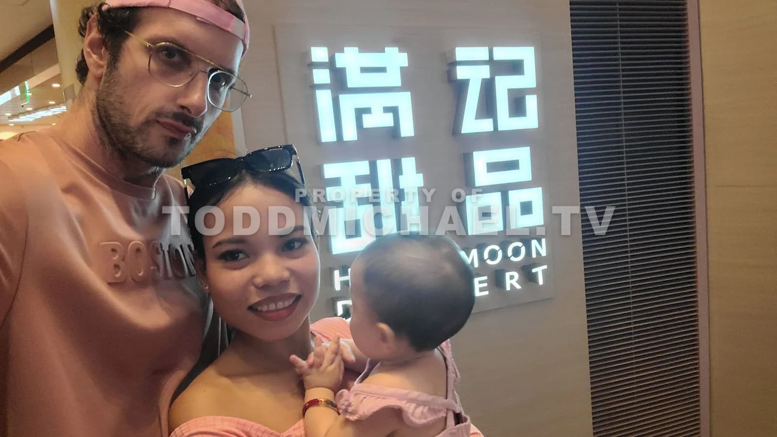 a family posing together with a baby in front of 'Honeymoon Dessert' signage.