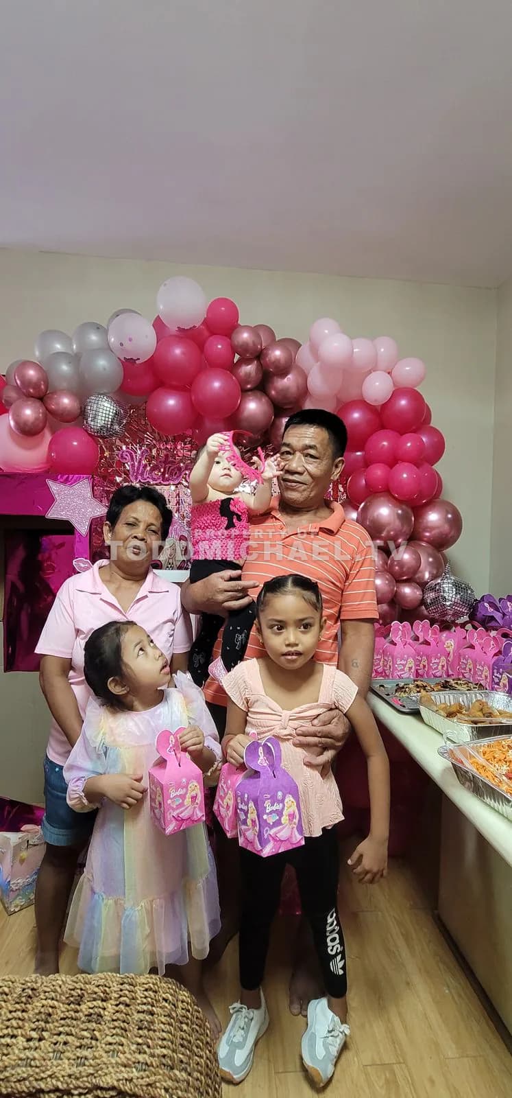 A family posing in front of a pink balloon arch with party decorations.